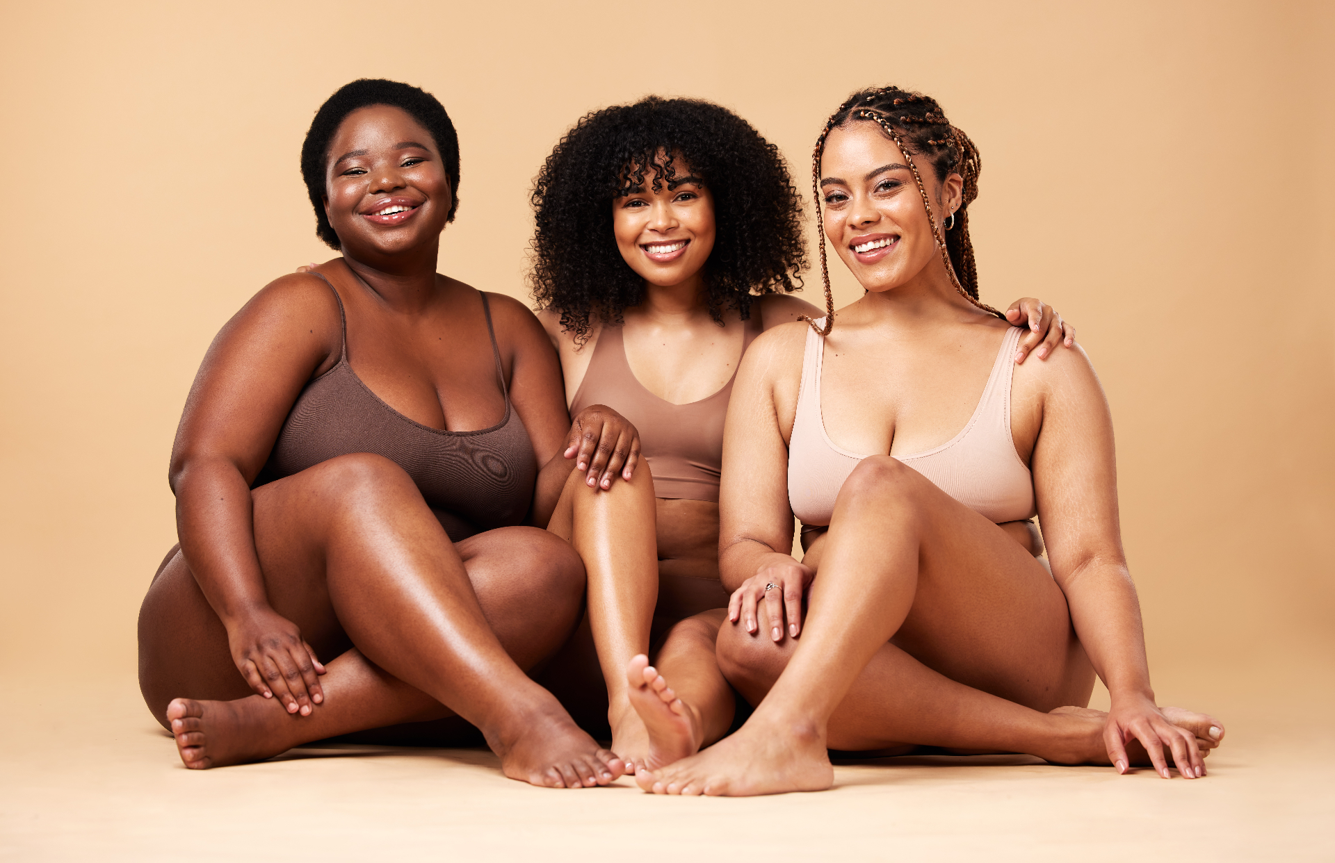 Three women of different sizes and skin tones sitting together, smiling with confidence