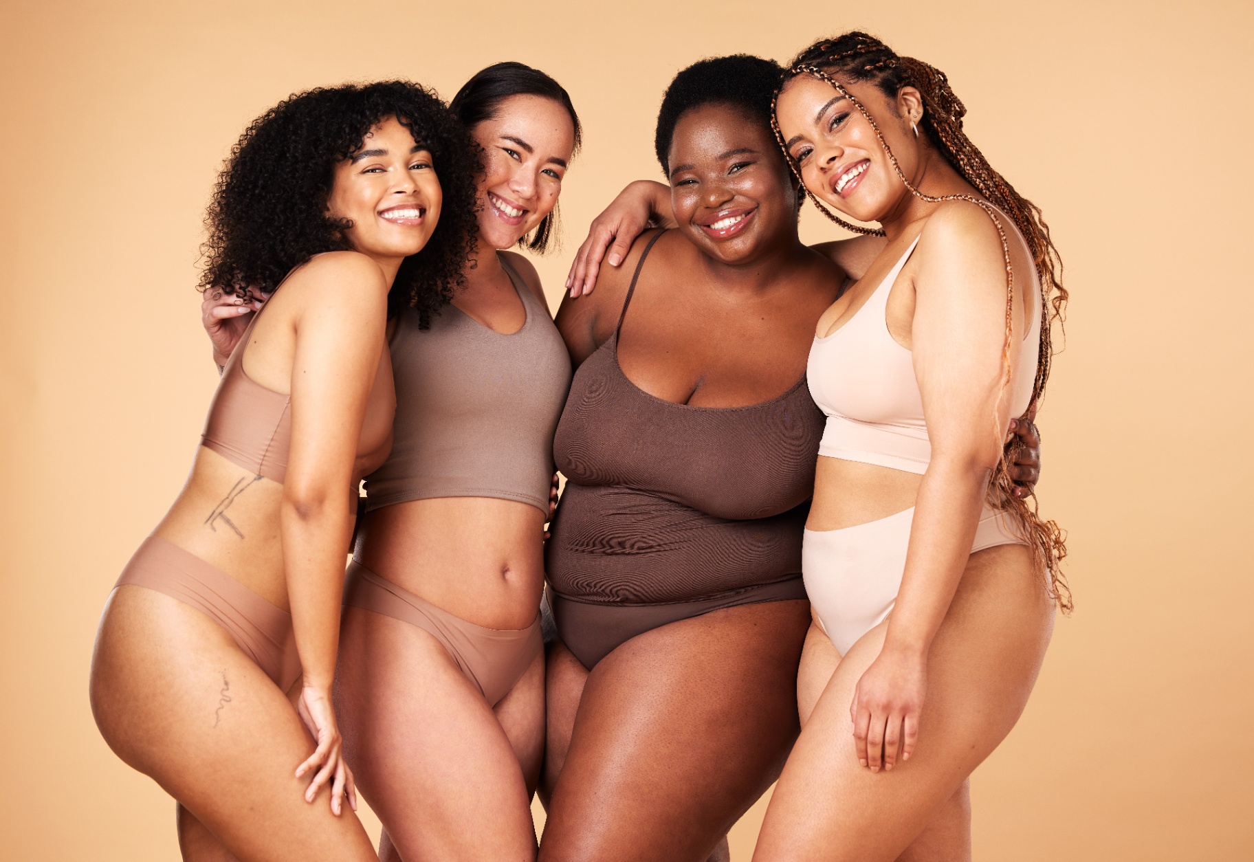 Four women of diverse ethnicities and body types embracing and smiling together